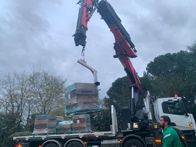 Camion grue déchargeant des palettes de tuiles sur un chantier de couverture en Dordogne
